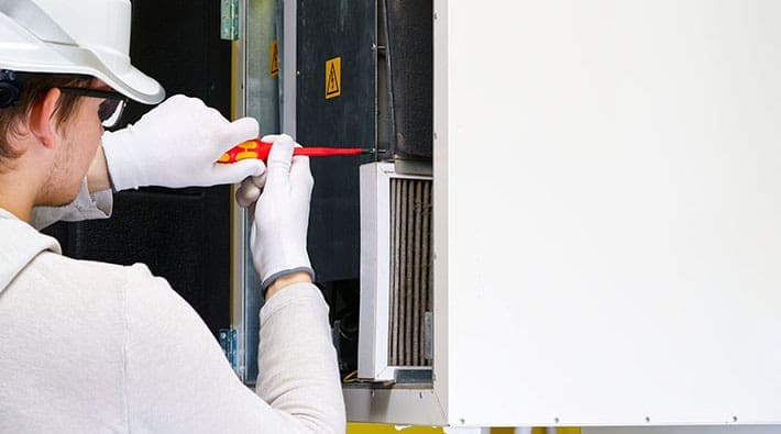 A service person uses a tool to access a furnace.